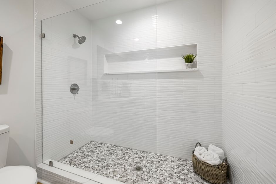 Sleek contemporary shower with glass panel, white walls, and mosaic tiles.